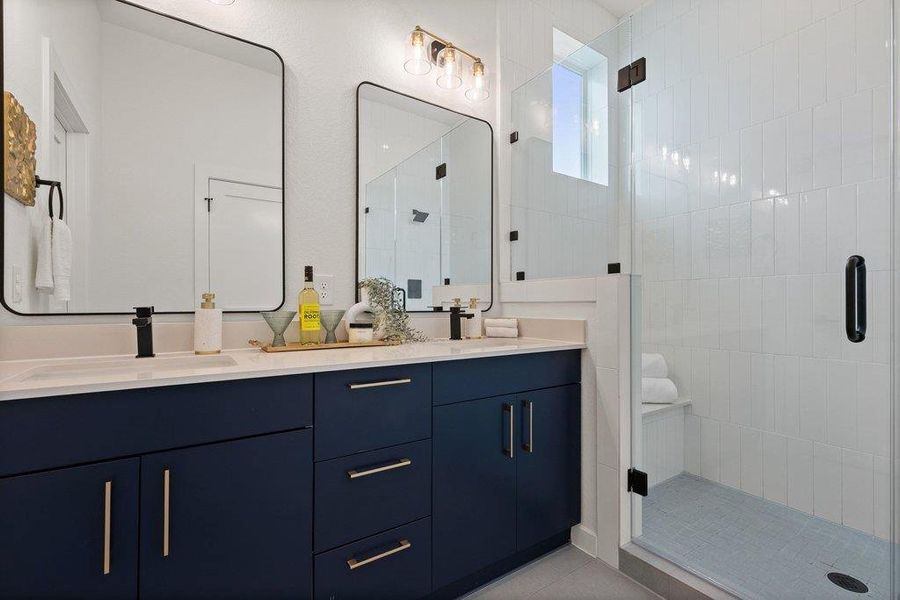 This well-appointed bathroom features a double vanity with dark blue cabinetry, light countertops, and individual mirrors