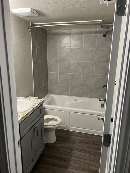 Bathroom featuring vanity, toilet,  shower combination, wood finished floors, and a textured ceiling