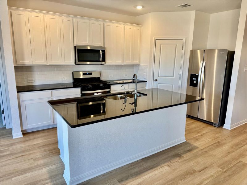 Kitchen with stainless steel appliances, decorative backsplash, white cabinetry, a kitchen island with sink, and light wood-type flooring Kitchen with stainless steel appliances, decorative backsplash, white cabinetry, a kitchen island with sink, and light wood-type flooring