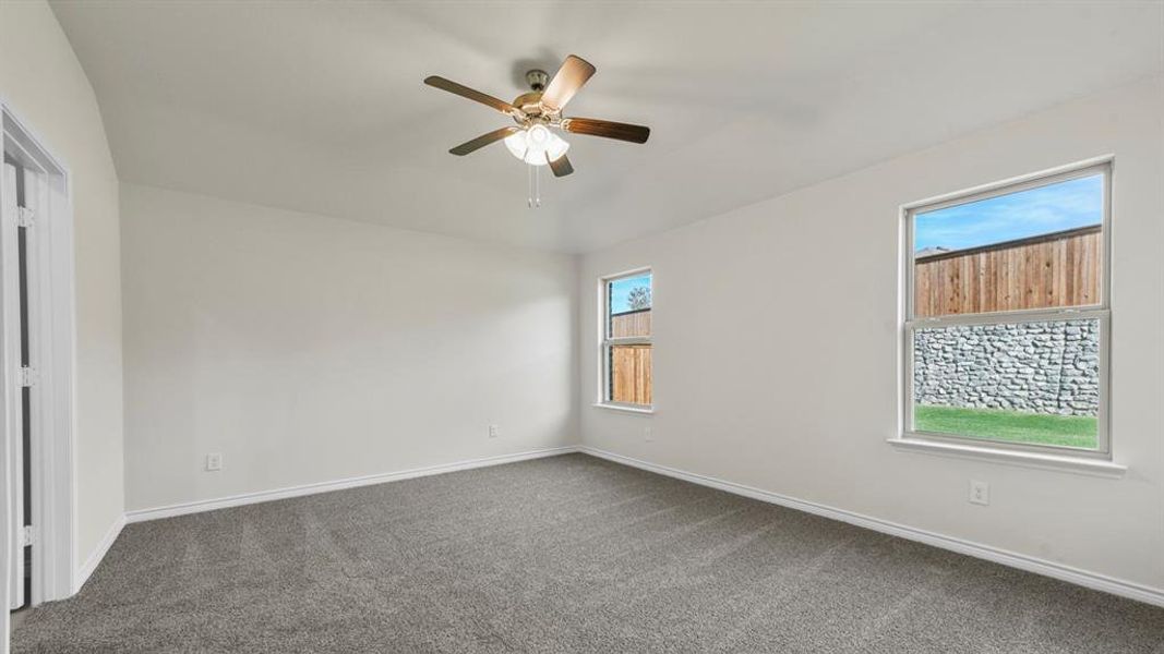 Spacious room with plush gray carpeting, crisp white walls, two windows, a ceiling fan with light fixture, and a white trim package