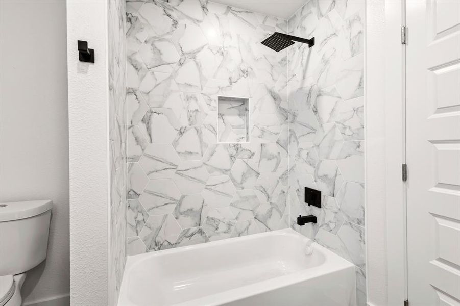 Bathroom featuring a bathtub with a black shower head, black faucet, and white and gray patterned tile surround