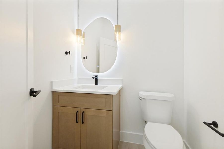 Modern powder room featuring a light wood-finish vanity with an integrated sink, a backlit irregular-shaped mirror, and sleek matte black fixtures Modern powder room featuring a light wood-finish vanity with an integrated sink, a backlit irregular-shaped mirror, and sleek matte black fixtures