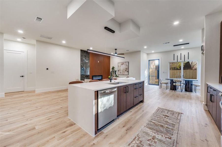 Kitchen with decorative light fixtures, a center island with sink, stainless steel dishwasher, modern cabinets, and light stone countertops