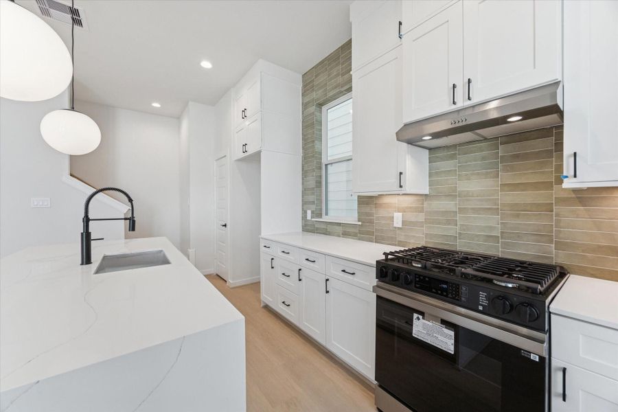An up-close shot highlights the kitchen’s sage green backsplash, quartz countertops, and floor-to-ceiling cabinets with under-cabinet lighting and soft-close drawers and doors, showcasing the thoughtful design and modern, functional finishes.