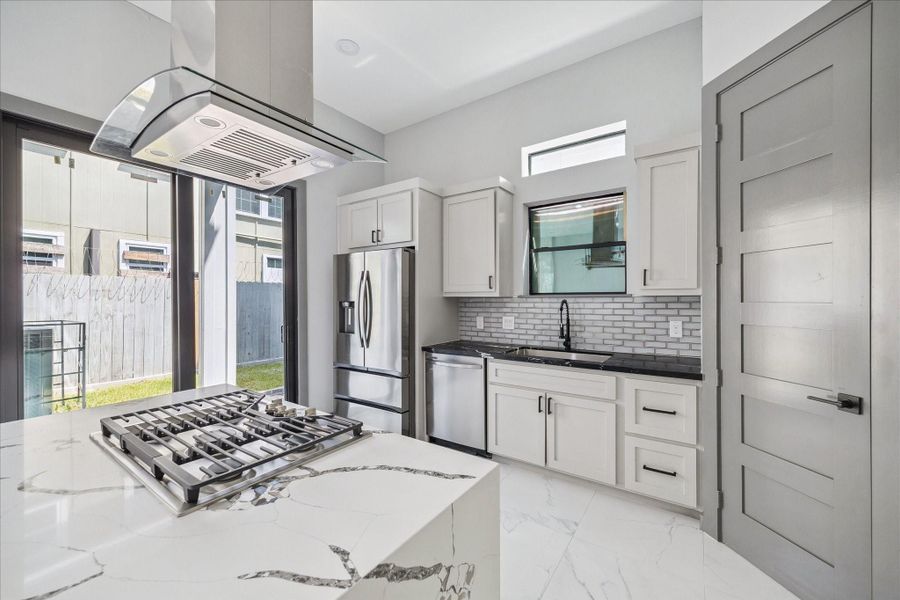 A well-planned kitchen design shines from the island view, where white cabinetry, a bold backsplash, and stainless steel appliances combine with natural light from the sink-side window for a bright, polished look.