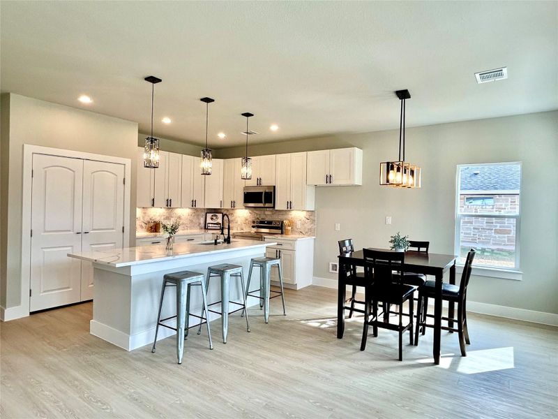 Kitchen with a breakfast bar area, white cabinets, pendant lighting, a kitchen island with sink, and stainless steel appliances