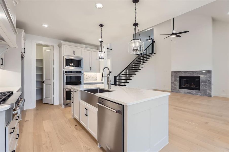 Kitchen featuring stainless steel appliances, sink, light hardwood / wood-style flooring, white cabinetry, and an island with sink