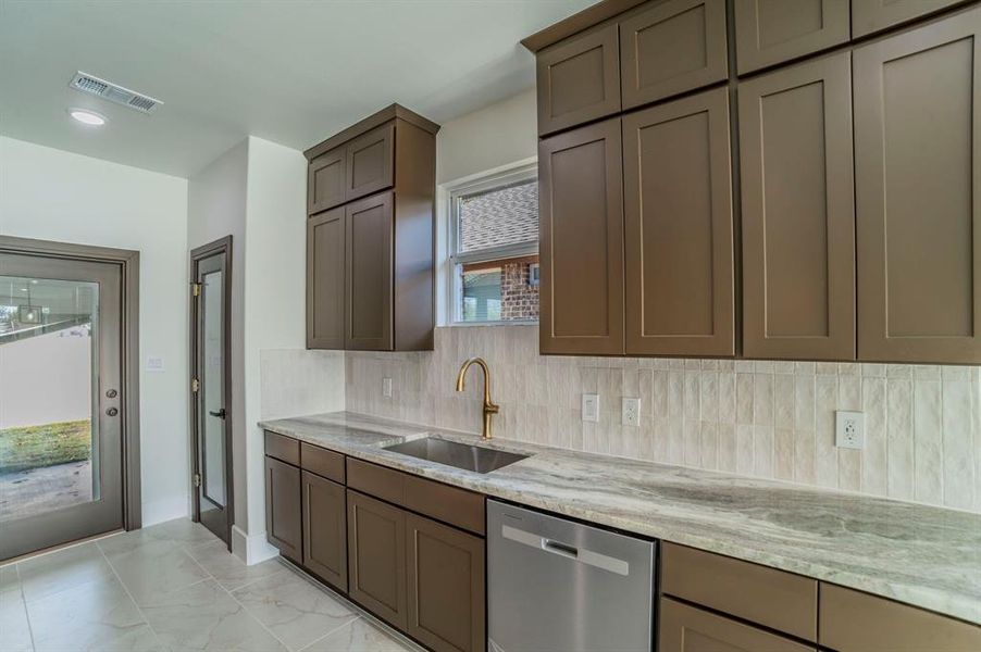 Kitchen with light stone counters, stainless steel dishwasher, light marble finish flooring, gray cabinets, and tasteful backsplash Kitchen with light stone counters, stainless steel dishwasher, light marble finish flooring, gray cabinets, and tasteful backsplash