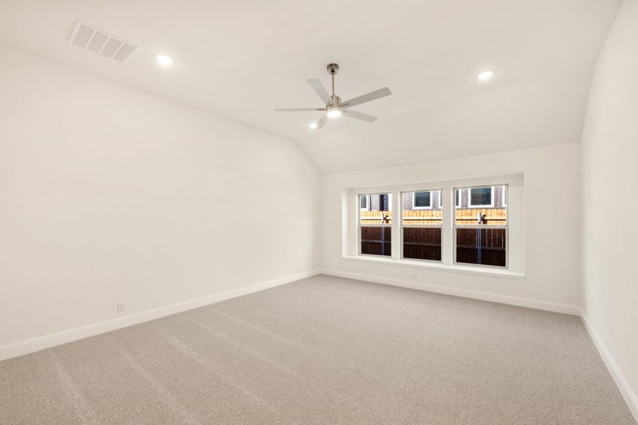 Empty bedroom with vaulted ceiling, ceiling fan, carpet flooring, and a wide four-panel window Empty bedroom with vaulted ceiling, ceiling fan, carpet flooring, and a wide four-panel window