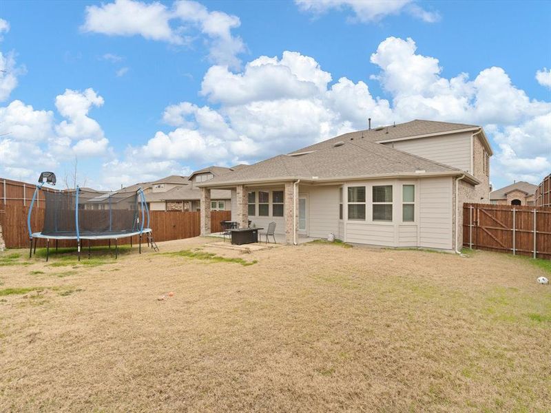 Back of property with a yard, a trampoline, and a fire pit