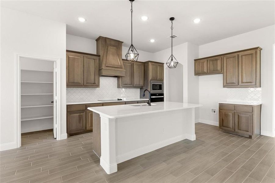 Kitchen with decorative backsplash, brown cabinets, pendant lighting, an island with sink, and recessed lighting Kitchen with decorative backsplash, brown cabinets, pendant lighting, an island with sink, and recessed lighting