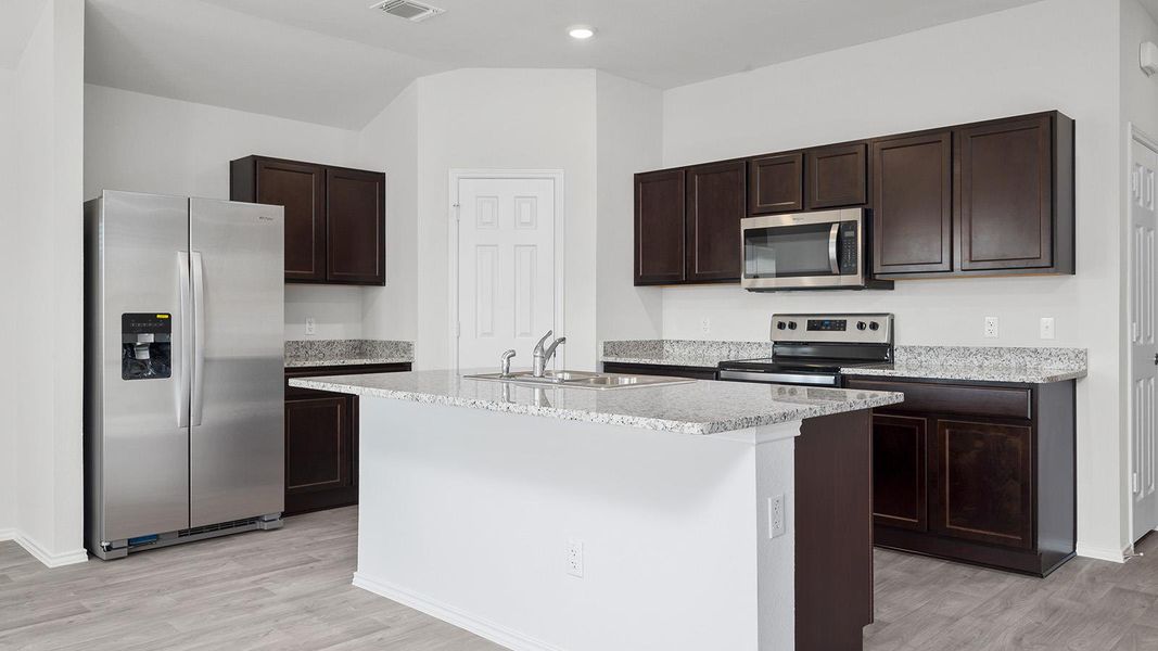 Kitchen with stainless steel appliances, dark wood finish cabinetry, a kitchen island with sink, light wood-style flooring, and light stone countertops