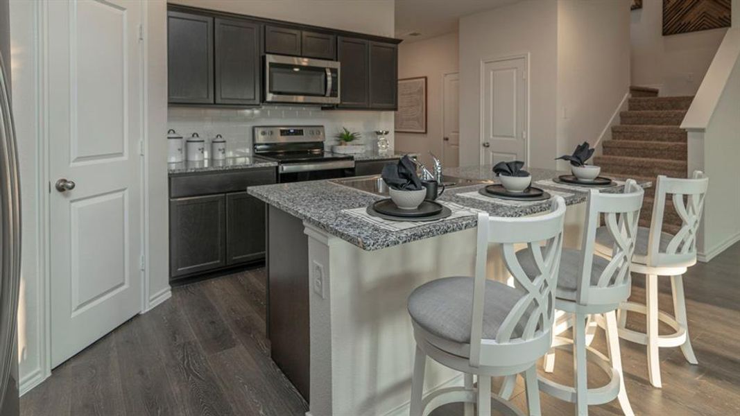 Kitchen featuring dark wood cabinetry, stainless steel appliances, a tile backsplash, and a central island with a granite countertop