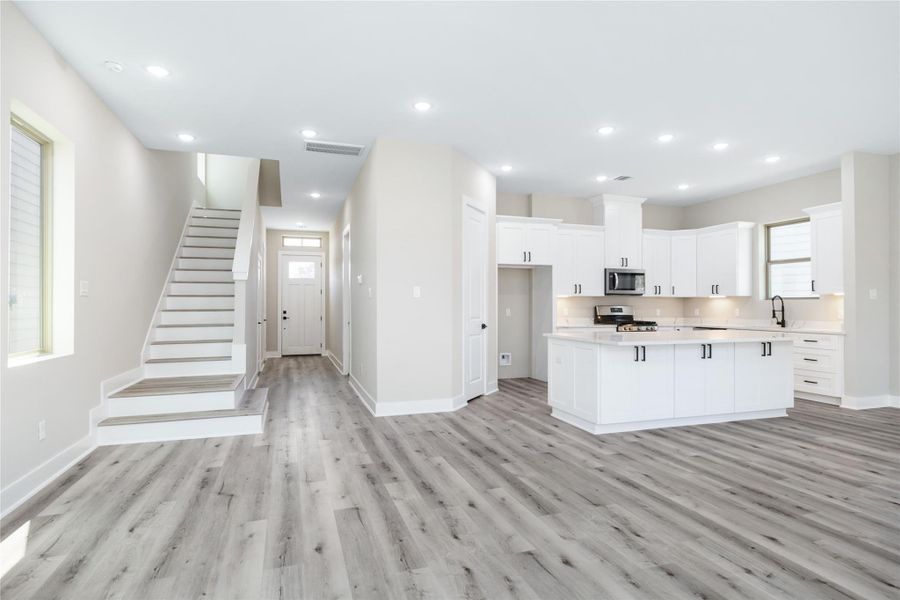 Featuring recessed lighting, crisp white cabinetry with bold black hardware, and luxurious vinyl plank flooring, this open-concept modern design exudes sophistication and a touch of elegance.