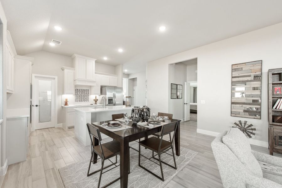 Open-concept dining area with dark wood table and chairs, adjacent to white kitchen with island and light wood floors