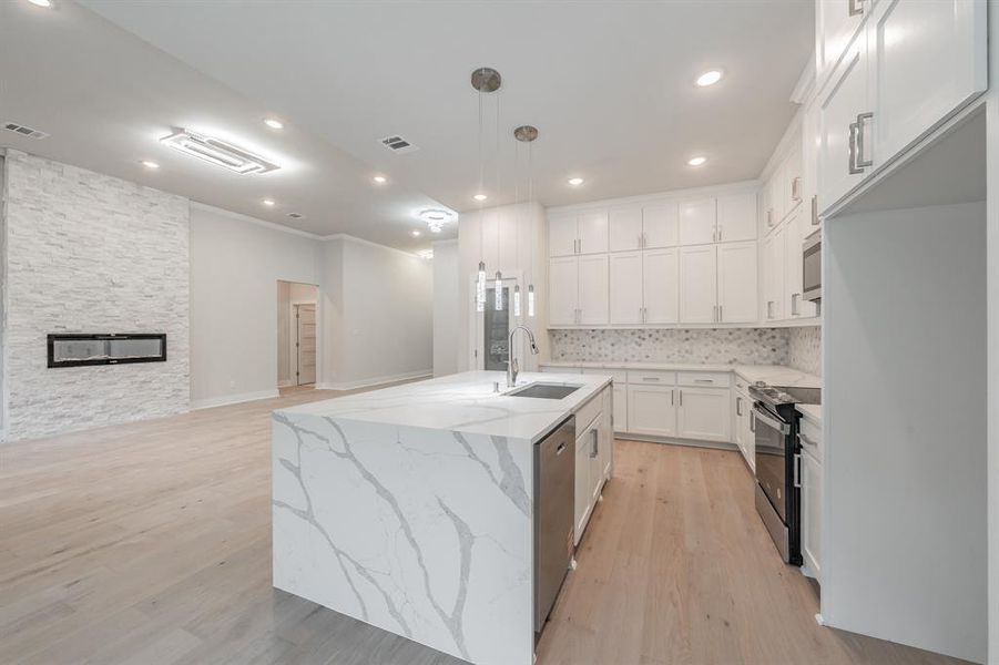 Kitchen with decorative backsplash, light wood finished floors, black range with electric cooktop, light stone countertops, and open floor plan