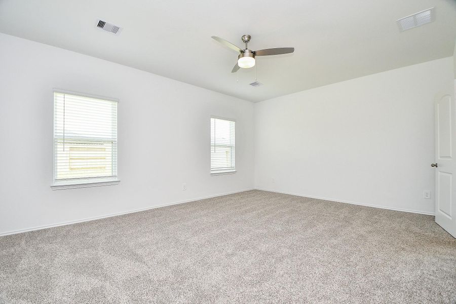 This spacious, bright room features neutral carpeting, two large windows for natural light, and a modern ceiling fan, creating a comfortable and inviting atmosphere.