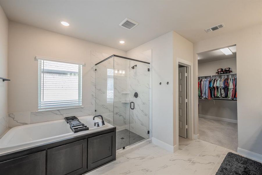 Bathroom with a garden tub, light marble finish floors, a marble finish shower, a walk in closet, and recessed lighting