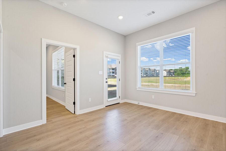 Spacious room featuring wood-finish flooring, a full-lite exterior door, and a large window with white blinds