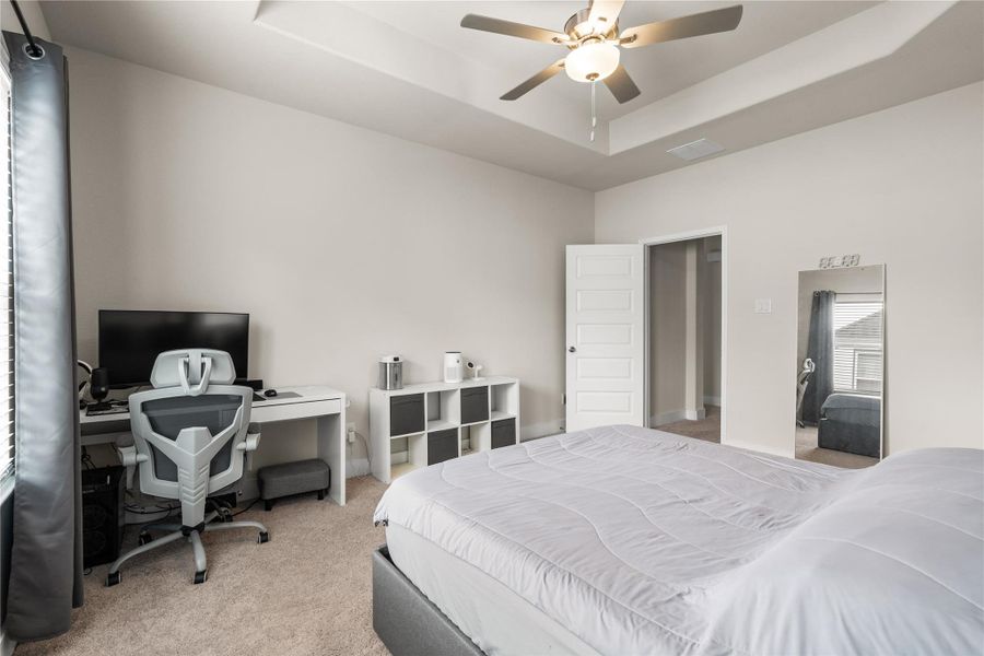 Elevated by a tray ceiling, the primary suite feels open and airy while offering ample space for both a sleeping area and a dedicated workspace or reading corner.