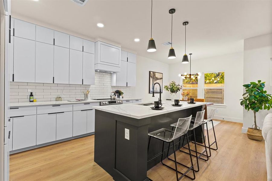 Kitchen featuring white cabinets, tasteful backsplash, a kitchen breakfast bar, hanging light fixtures, and light wood-type flooring