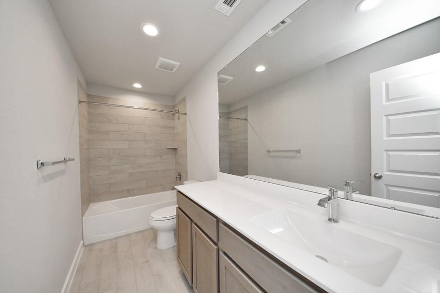 Secondary bath features tile flooring, bath/shower combo with tile surround, light stained wood cabinets, beautiful light countertop. Sample photo of completed home with similar floor plan. Actual colors and selections may vary.
