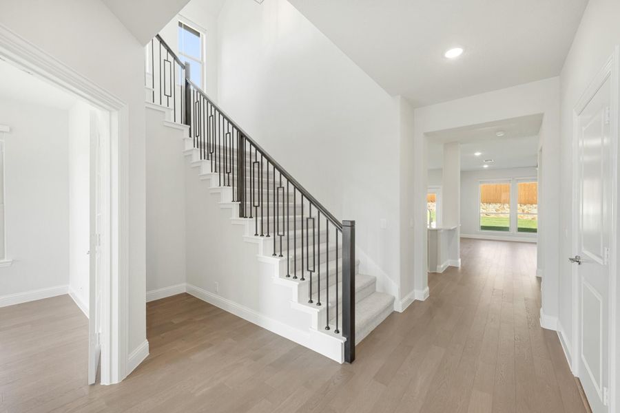 Bright entryway with staircase featuring black iron balusters, white walls, and hardwood floors leading to main living area.
