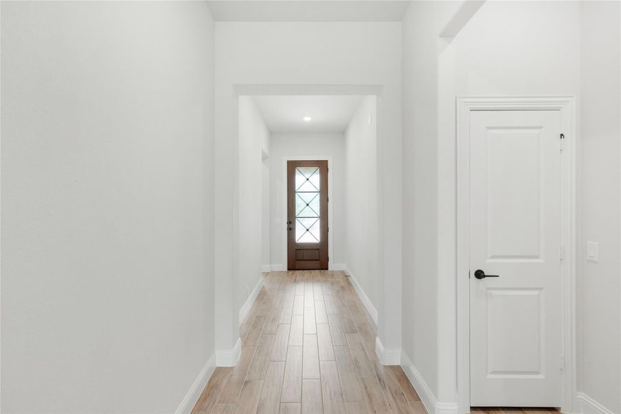Hallway with light wood floors, white walls, and wood front door with glass panels