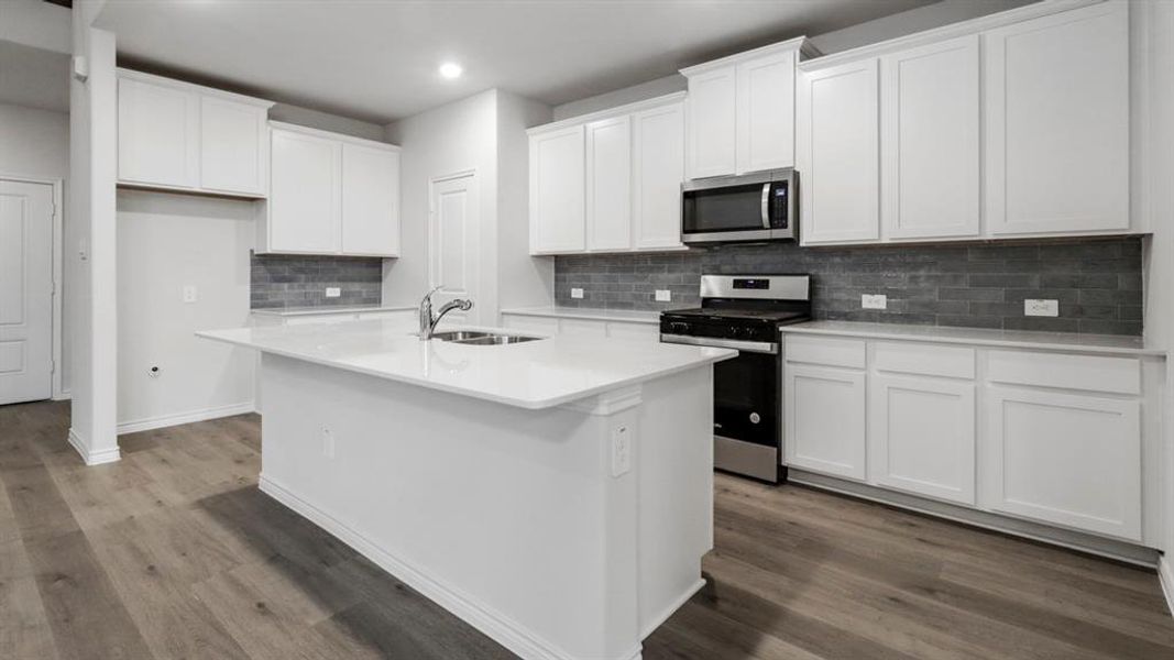 Kitchen with stainless steel appliances, white cabinetry, a center island with sink, decorative backsplash, and light stone countertops Kitchen with stainless steel appliances, white cabinetry, a center island with sink, decorative backsplash, and light stone countertops