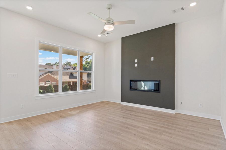 Integrated linear fireplace with a dark accent wall, recessed ceiling lighting, wood-finish flooring, and a ceiling fan