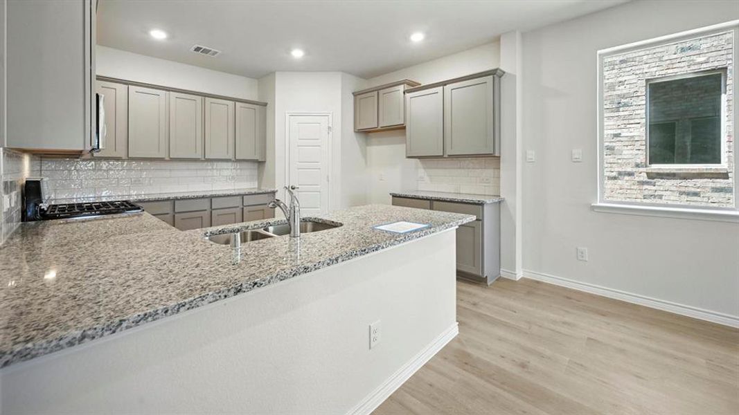 Kitchen featuring gray cabinets, decorative backsplash, a peninsula, light stone countertops, and light wood finished floors
