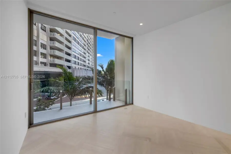 Floor-to-ceiling sliding glass doors, herringbone-patterned wood-finish flooring, recessed lighting, and a private balcony with glass railing