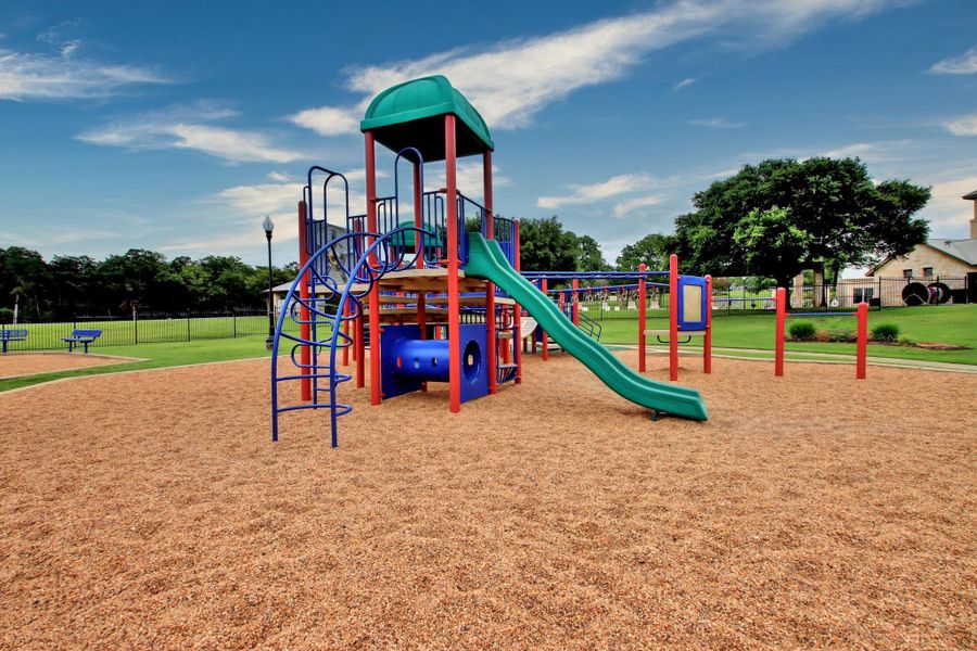 Recreational area featuring a colorful playground with slides and climbing structures, surrounded by a wood chip surface