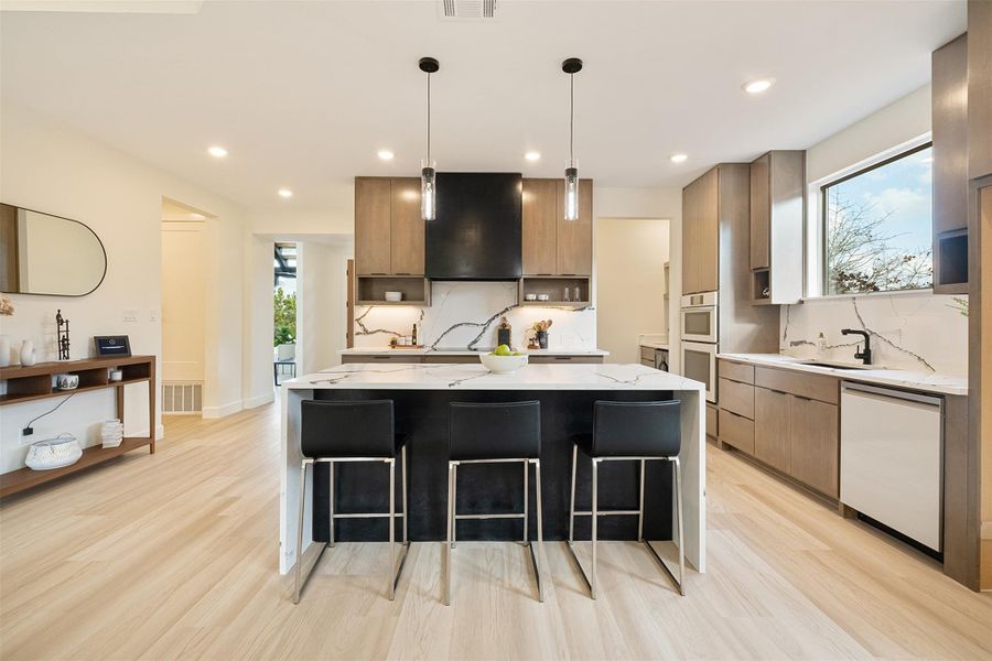 Kitchen with light stone countertops, modern cabinets, an island with sink, dishwasher, and a kitchen bar