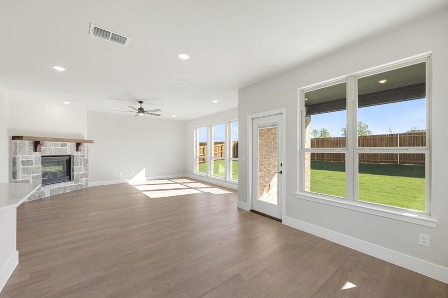 Open living room with stone fireplace, hardwood floors, ceiling fan, and back door with yard view