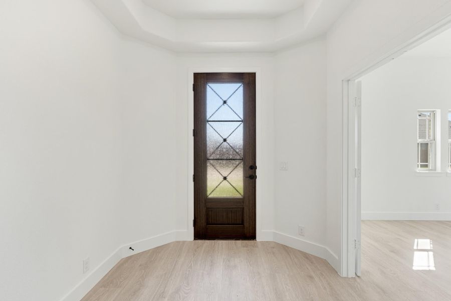 Entryway with dark wood front door featuring glass panels, tray ceiling, and light hardwood floors