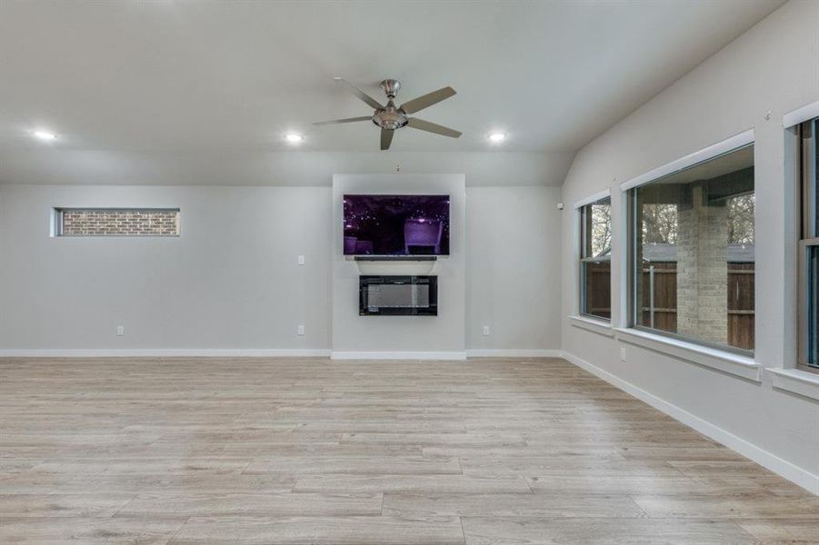 Unfurnished living room featuring light wood-style flooring, a ceiling fan, recessed lighting, and a glass covered fireplace Unfurnished living room featuring light wood-style flooring, a ceiling fan, recessed lighting, and a glass covered fireplace