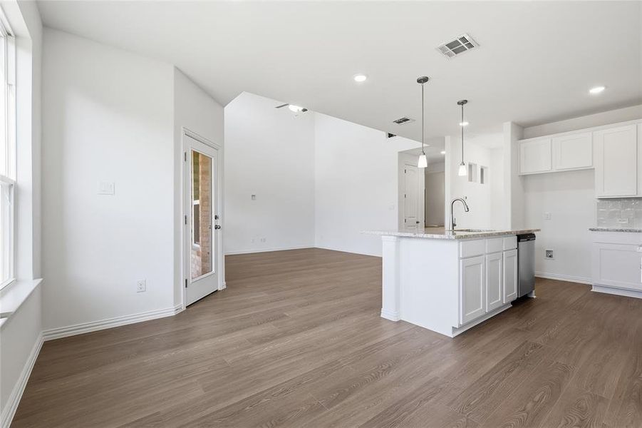 Kitchen with white cabinetry, light stone counters, pendant lighting, an island with sink, and dark wood finished floors
