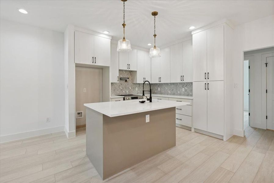 Kitchen featuring a kitchen island with sink, hanging light fixtures, light hardwood / wood-style flooring, and white cabinets