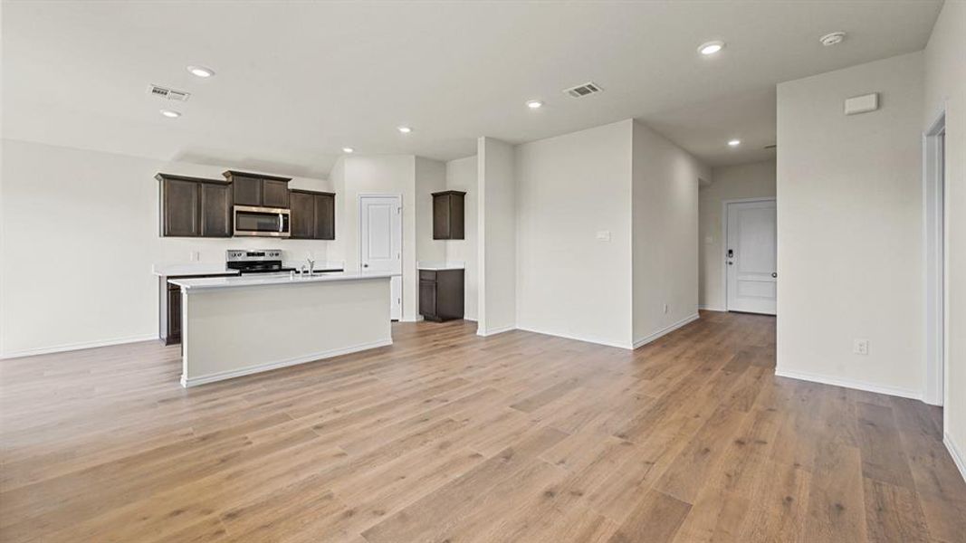Kitchen with light countertops, open floor plan, a center island with sink, dark wood finish cabinetry, and recessed lighting