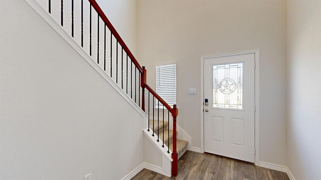 The property features a staircase with a wooden handrail and black balusters, and a front entry door with decorative glass