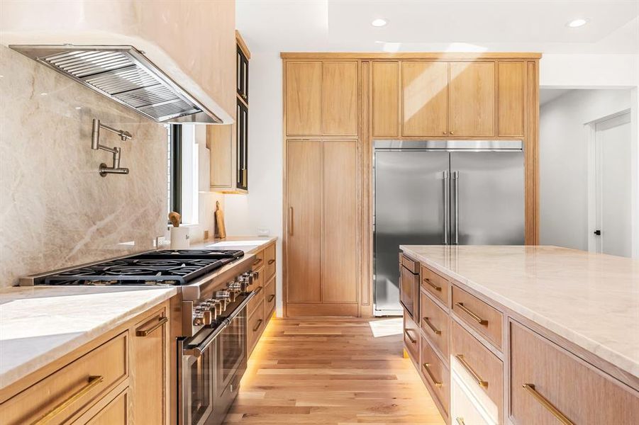 Kitchen with light stone countertops, high quality appliances, light brown cabinetry, range hood, and recessed lighting Kitchen with light stone countertops, high quality appliances, light brown cabinetry, range hood, and recessed lighting