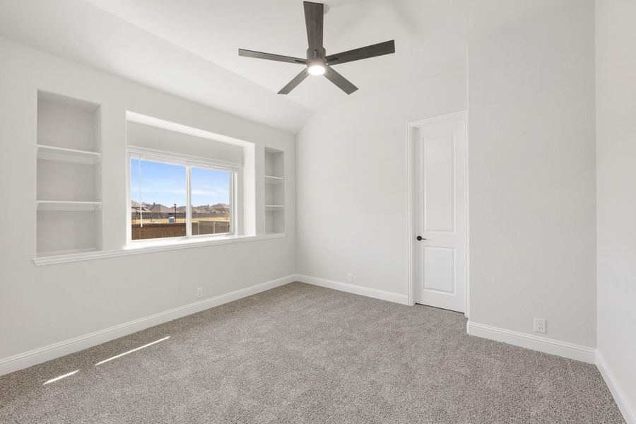 Empty bedroom with vaulted ceiling, ceiling fan, built-in shelves, and carpet flooring Empty bedroom with vaulted ceiling, ceiling fan, built-in shelves, and carpet flooring