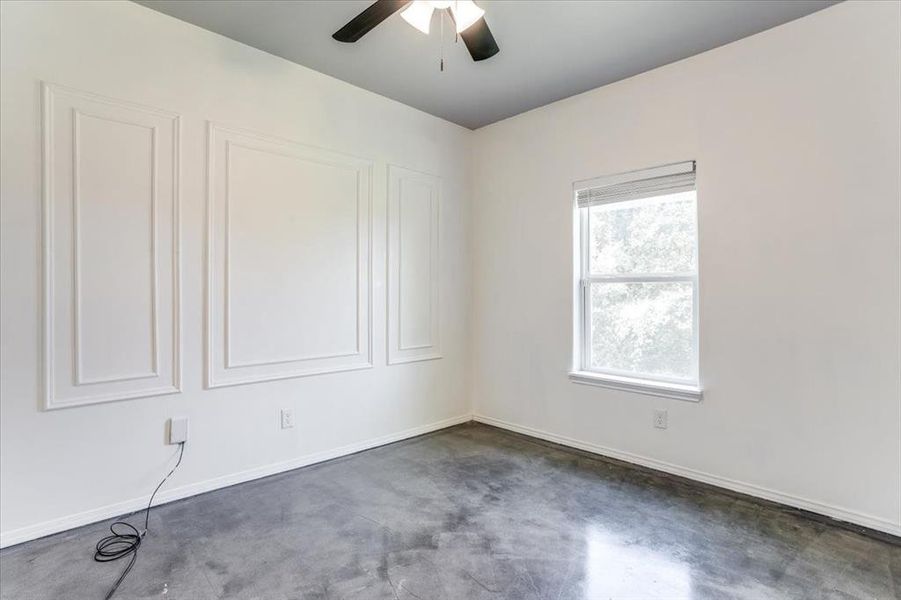 Room featuring accent wall with decorative wall molding, a single window with blinds, dark-toned ceiling fan, and concrete flooring