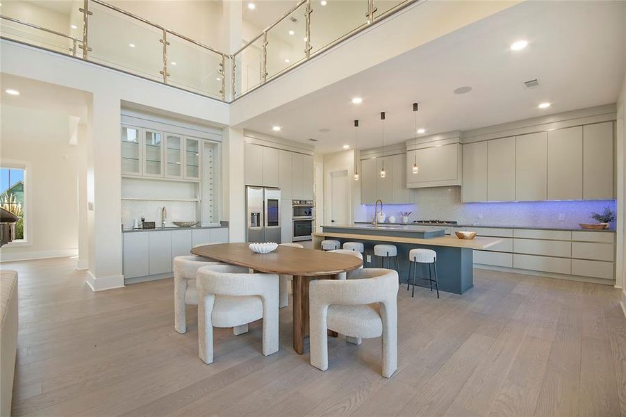 Dining room with light wood-style floors, a towering ceiling, and recessed lighting Dining room with light wood-style floors, a towering ceiling, and recessed lighting