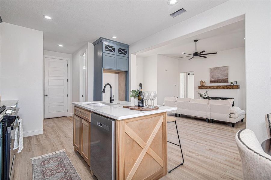 Kitchen with open floor plan, light wood-type flooring, appliances with stainless steel finishes, a ceiling fan, and an island with sink
