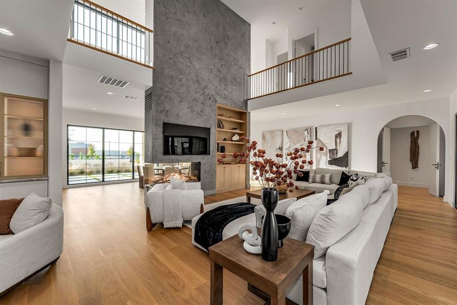Living room featuring arched walkways, a towering ceiling, a multi sided fireplace, recessed lighting, and light wood-type flooring Living room featuring arched walkways, a towering ceiling, a multi sided fireplace, recessed lighting, and light wood-type flooring