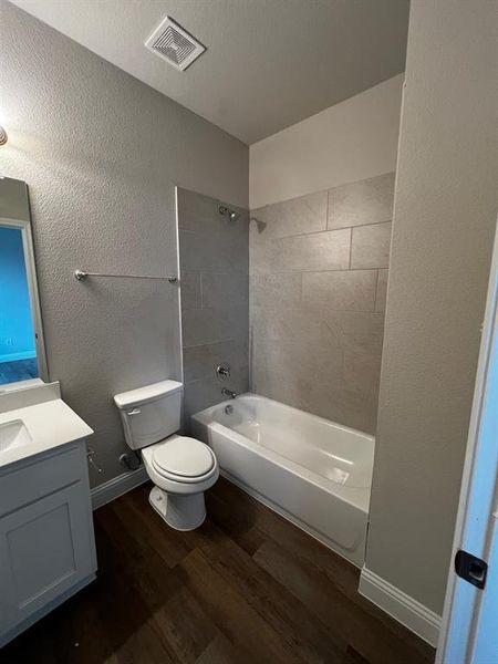 Full bathroom with wood-type flooring, tiled shower / bath combo, vanity, toilet, and a textured ceiling