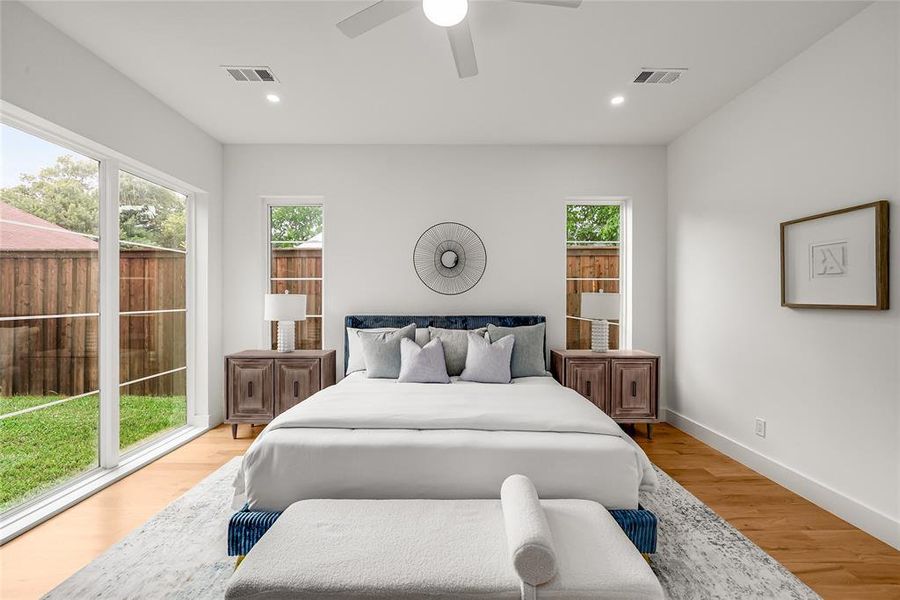 Spacious bedroom with natural wood-finish flooring, a contemporary ceiling fan, recessed lighting, and expansive glass sliding doors providing exterior access