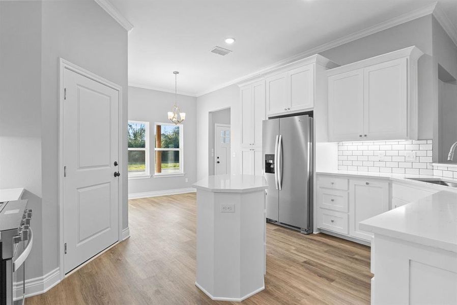 Kitchen featuring ornamental molding, white cabinets, stainless steel appliances, decorative light fixtures, and a chandelier